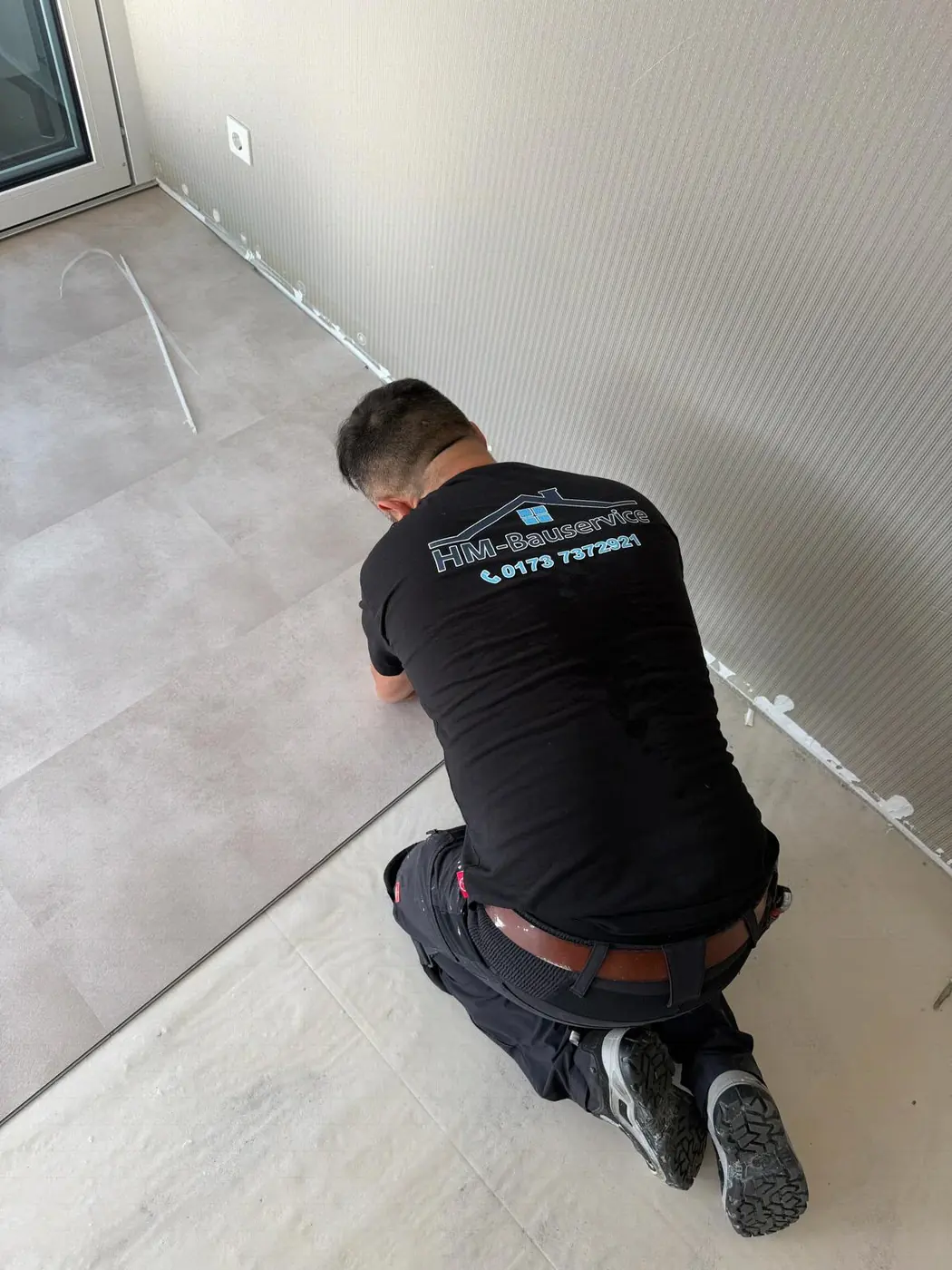 Handwerker kniet bei der Verlegung eines hellen Bodenbelags