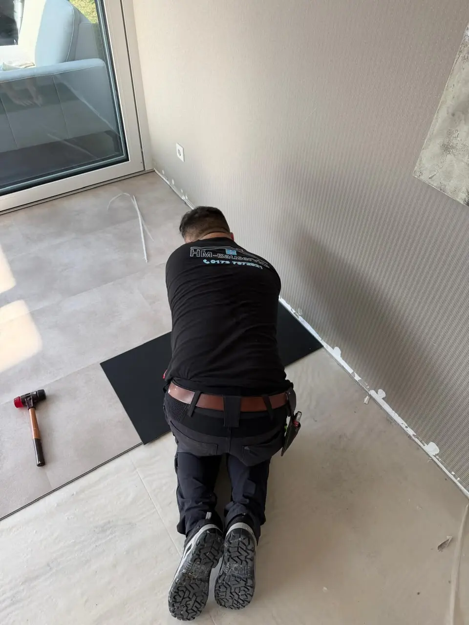 Handwerker verlegt hellen Boden in einem Raum mit großer Fensterfront