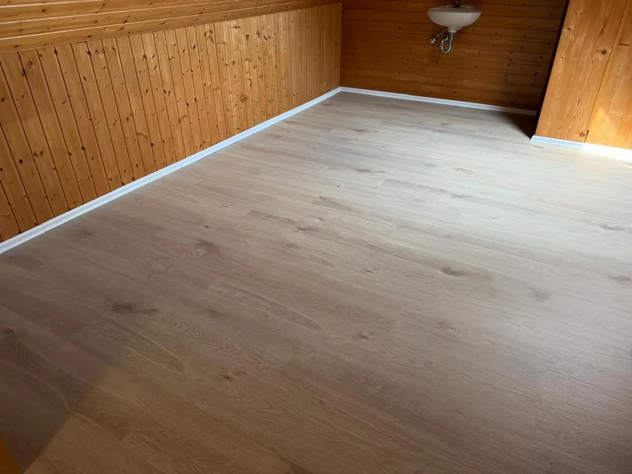 Raum mit Holzverkleidung an der Wand und neu verlegtem Boden